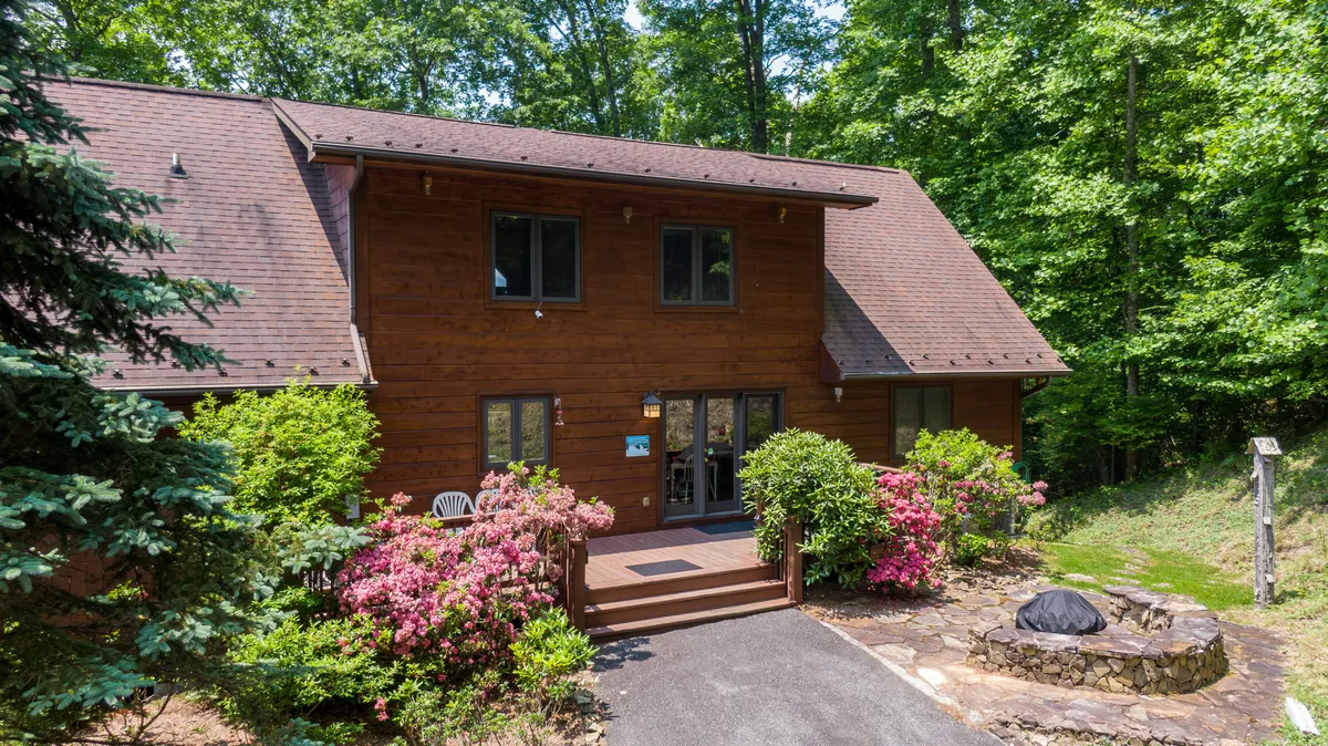 The cabin’s exterior, surrounded by lush greenery and flowering plants, with a welcoming porch and a cozy fire pit area. The scene captures a family-friendly atmosphere, inviting both people and pets to enjoy the outdoors together.