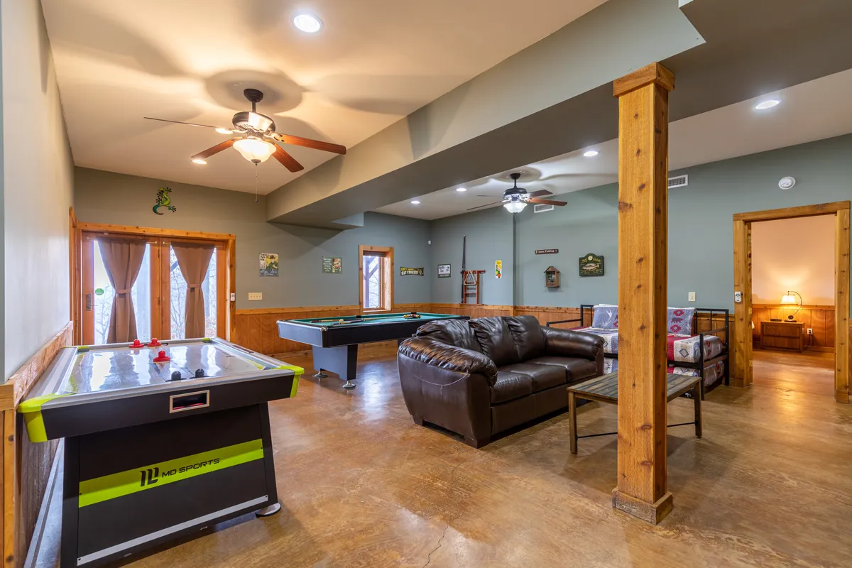 A spacious, lively entertainment area with a pool table and air hockey table, a leather sofa, rustic wood beams, and decorative wall art. The setup invites group play and relaxed socializing, embodying an energetic, celebratory mood.