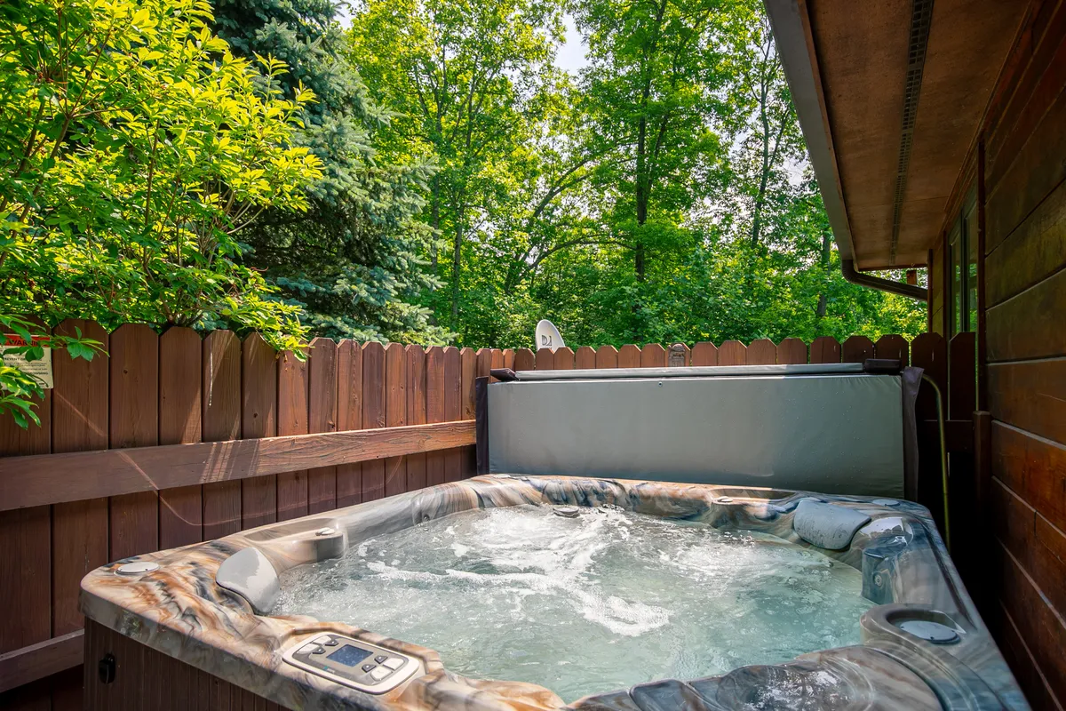 This image features a hot tub set on a wooden deck, nestled amidst lush greenery with a wooden fence providing privacy. The tranquil outdoor ambiance is perfect for unwinding while enjoying natural surroundings, suggesting a premium amenity and a space for relaxation after a day of family adventures.