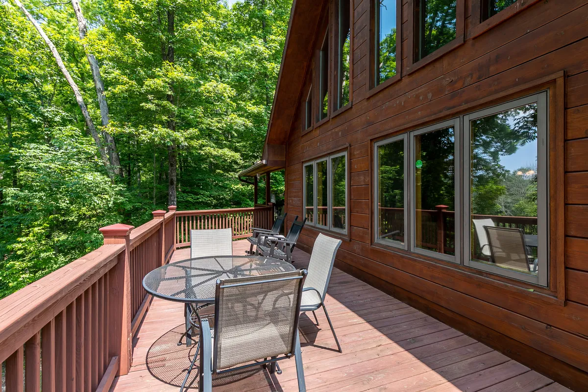 A tranquil wooden deck nestled among trees, featuring an outdoor dining table and chairs. The lush greenery surrounding the deck provides a sense of privacy and immersion in nature, perfect for gatherings or peaceful relaxation.