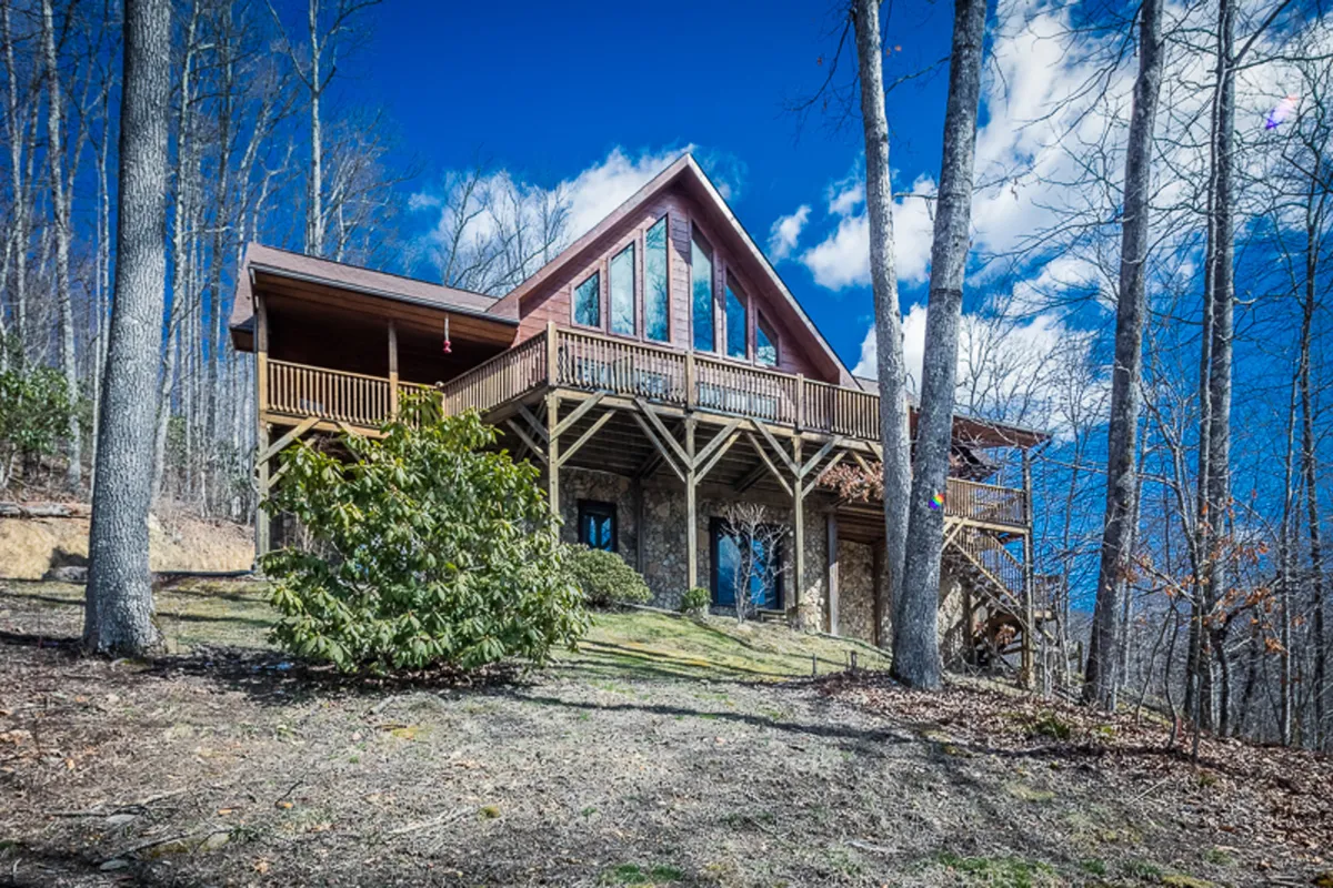 This image features the A-frame architecture of Raccoon's Paw Lodge, surrounded by tall trees and a wooden deck that invites outdoor relaxation. The large windows blur the boundaries between indoor comfort and the beautiful mountain setting, emphasizing the lodge’s connection to nature.