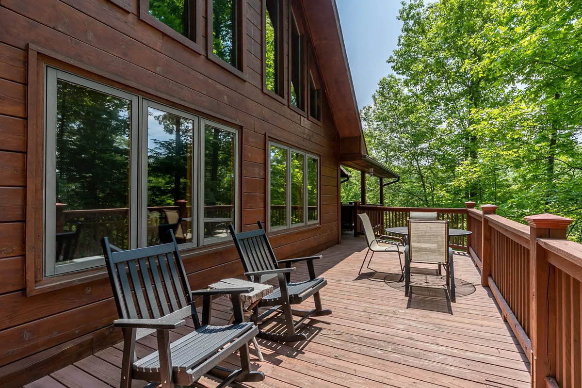 A spacious wooden deck furnished with classic rocking chairs overlooks a tranquil forested setting. Large windows on the cabin invite plenty of natural light and visually connect the indoors with the surrounding outdoors. The atmosphere is peaceful, perfect for relaxing with pets while enjoying the sights and sounds of nature.