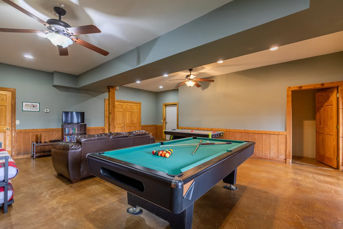 An interior recreation space featuring a pool table, a leather couch, and an entertainment center. The area is designed for playing games, socializing, or watching TV, encapsulating the lively, family-friendly spirit of the cabin’s amenities.