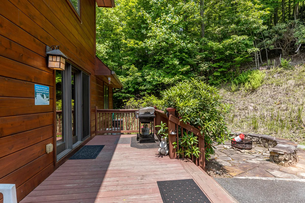 A spacious wooden deck is shown with a grill, stone fire pit, and abundant greenery all around. The scene suggests both daytime and evening outdoor experiences, from cookouts to gatherings under the stars, encapsulating the social and recreational possibilities right at the lodge.
