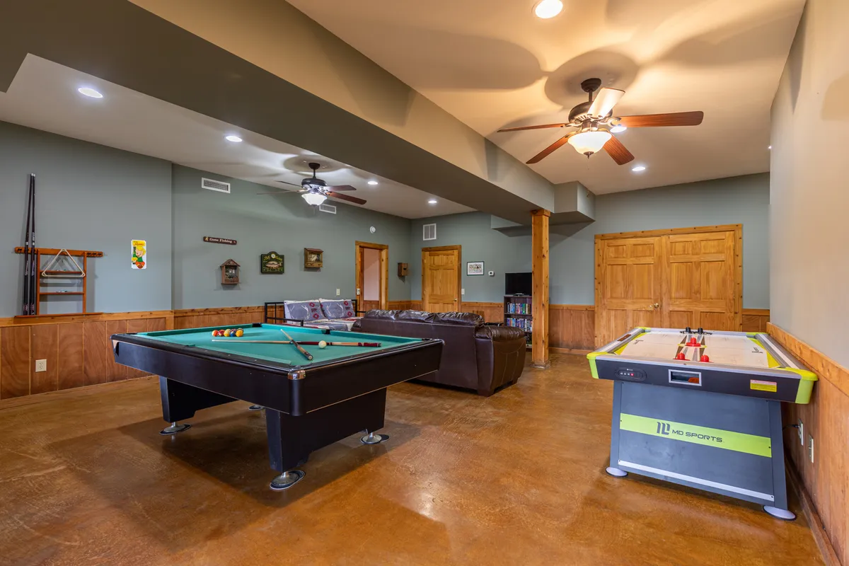 A game room featuring both a pool table and an air hockey table, with a comfortable sofa along one wall. The wooden walls and cozy furnishings create a relaxed, playful atmosphere perfect for gatherings and friendly competition.